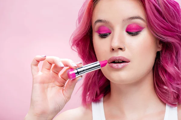 young woman with colorful hair holding lipstick isolated on pink