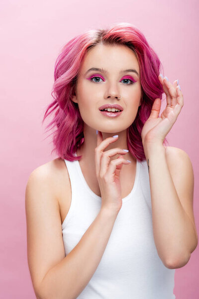 young woman with colorful hair and makeup posing with hands near face isolated on pink