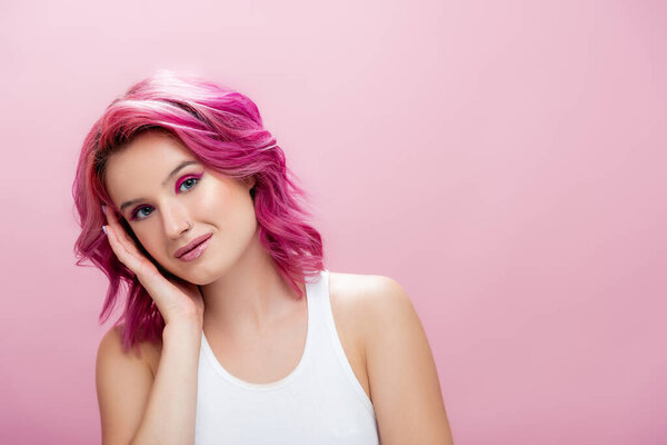 young woman with colorful hair and makeup touching face isolated on pink