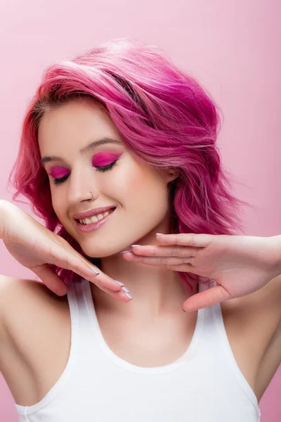 young woman with colorful hair and makeup posing with hands near face and closed eyes isolated on pink