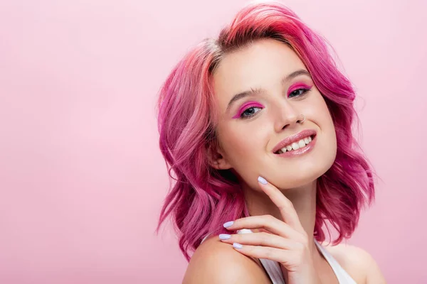 young woman with colorful hair and makeup posing with hand near face isolated on pink