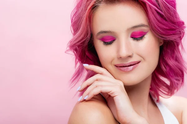 young woman with colorful hair and makeup posing with hand near face isolated on pink