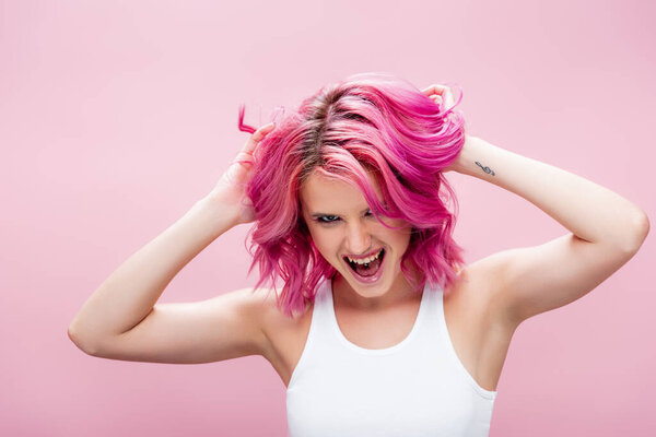 excited young woman touching colorful hair isolated on pink