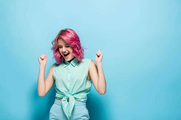 young woman with pink hair rejoicing on blue background