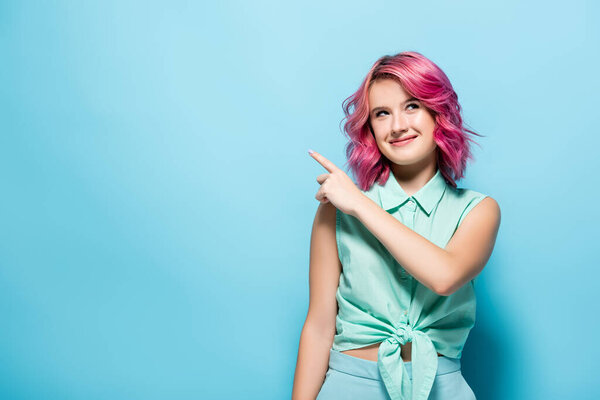 young woman with pink hair pointing aside on blue background