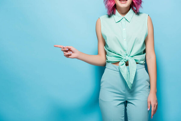 cropped view of young woman with pink hair pointing aside on blue background