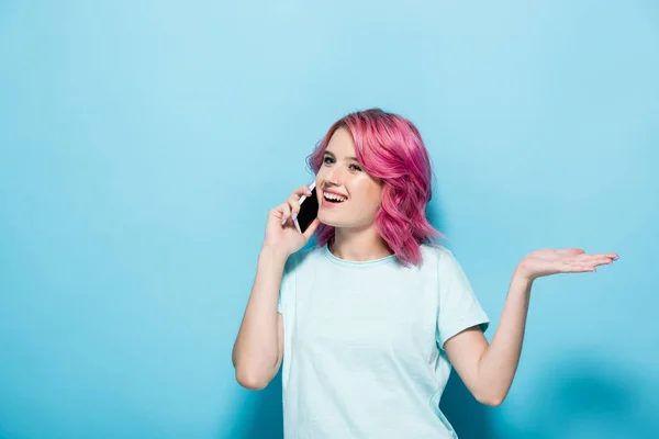 有一头粉色头发的年轻女人在智能手机上说话 蓝色背景上做手势 — 图库照片