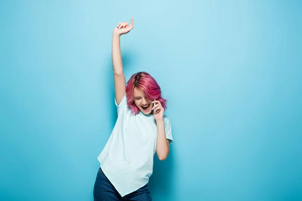 Збуджена Молода Жінка Рожевим Волоссям Розмовляє Смартфоні Піднятою Рукою Синьому — стокове фото
