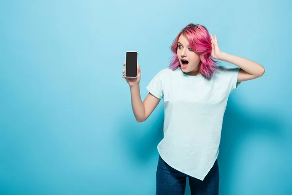 拥有粉色头发的年轻女性震惊地拿着蓝底屏幕的智能手机 — 图库照片