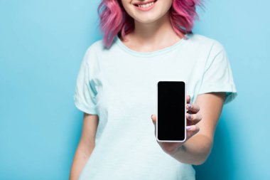 Pembe saçlı, elinde akıllı bir telefonla mavi arka planda boş ekranlı genç bir kadın görüntüsü.
