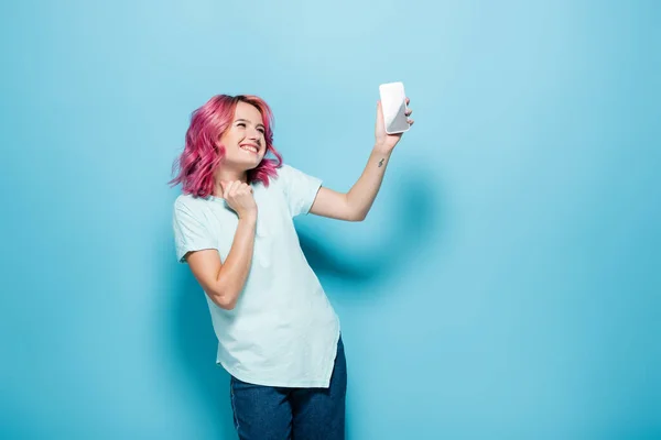 Młoda Kobieta Różowymi Włosami Trzyma Smartfon Niebieskim Tle — Zdjęcie stockowe