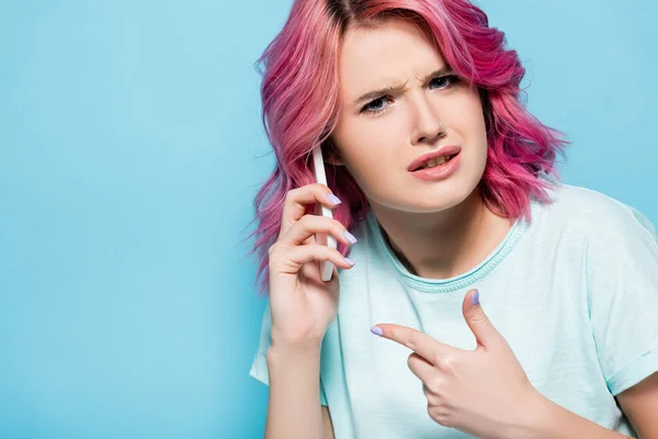 Confused Young Woman Pink Hair Pointing Smartphone Isolated Blue — Stock Photo, Image