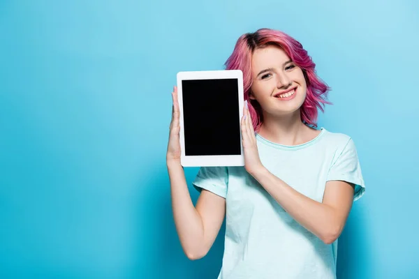 粉红头发的年轻女子展示数码平板电脑 蓝底上有空白屏幕 — 图库照片