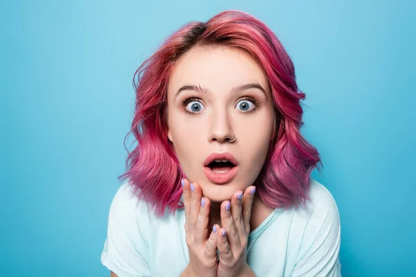 scared young woman with pink hair on blue background