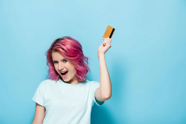 Podekscytowana Młoda Kobieta Różowymi Włosami Trzyma Kartę Kredytową Niebieskim Tle — Zdjęcie stockowe