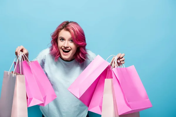 Збуджена Молода Жінка Рожевим Волоссям Тримає Сумки Покупок Посміхається Синьому — стокове фото
