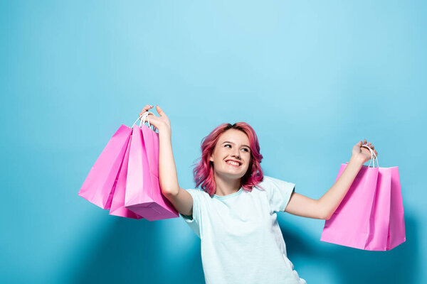 молодая женщина с розовыми волосами держит сумки с покупками и улыбается на синем фоне