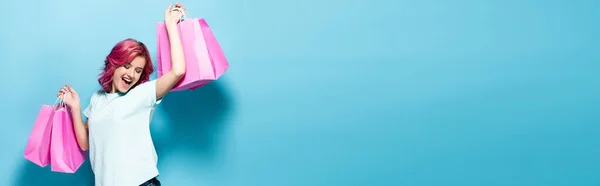 ピンクの髪をした若い女性が買い物袋を持っていて青い背景で笑ってパノラマ撮影 — ストック写真