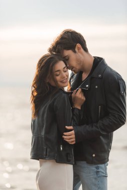 Brunette woman in dress and leather jacket standing near boyfriend and sea clipart