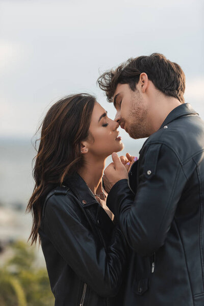 Young couple in leather jackets kissing with closed eyes outdoors 