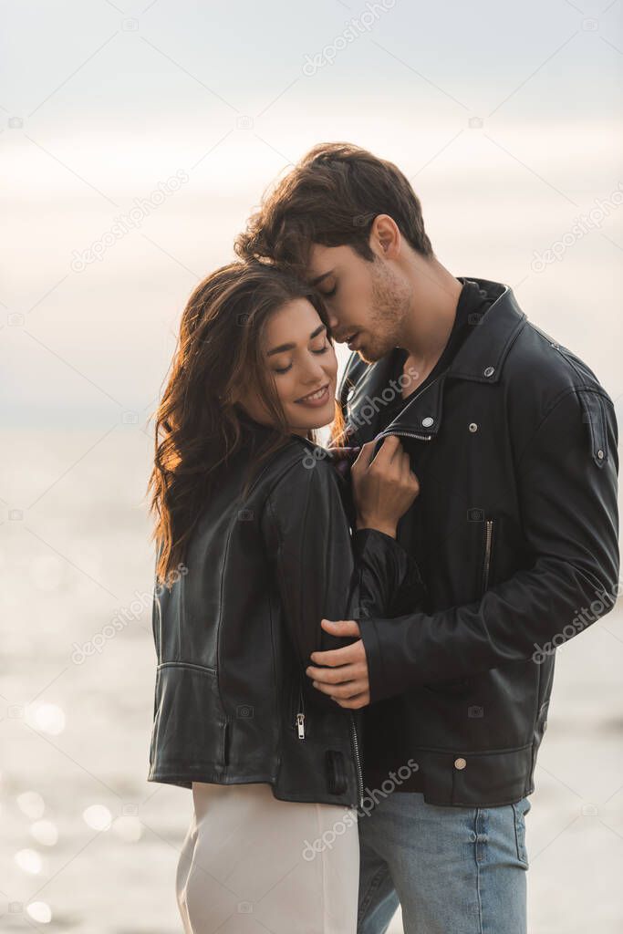 Brunette woman in dress and leather jacket standing near boyfriend and sea