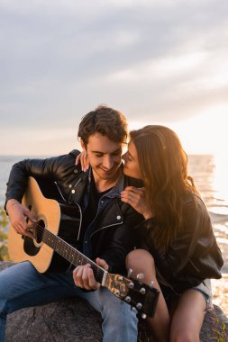 Seçici odak noktası, gün batımında erkek arkadaşının akustik gitar çalması. 