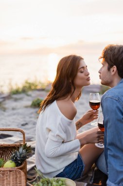 Plajda piknik yaparken bir kadeh şarap içerken öpüşen genç çiftin seçici odak noktası. 