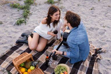 Piknik sırasında sahilde oturan şarap ve akustik gitarlı çift manzarası 