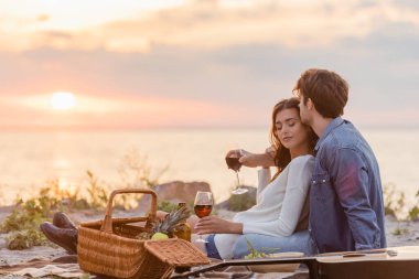 Akşamları plajda piknik yaparken ellerinde şarap bardakları olan seçici bir çift. 
