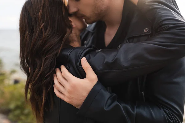 在海滩上亲吻和拥抱穿着皮夹克的黑发女友的男人 — 图库照片