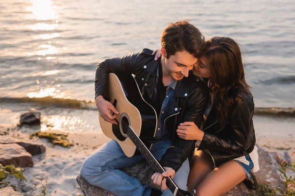 傍晚时分 布鲁内特的女人抱着男朋友 穿着带着音响吉它的皮夹克在海滨散步 — 图库照片