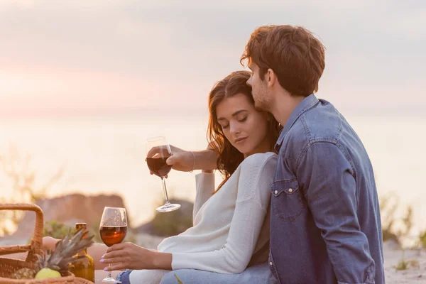 男子在海滩野餐时用酒杯拥抱女友的选择性焦点 — 图库照片