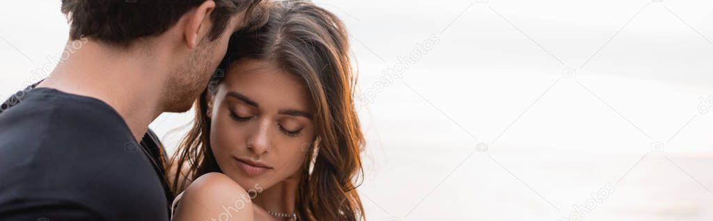 Panoramic shot of man standing near brunette girlfriend and sea 