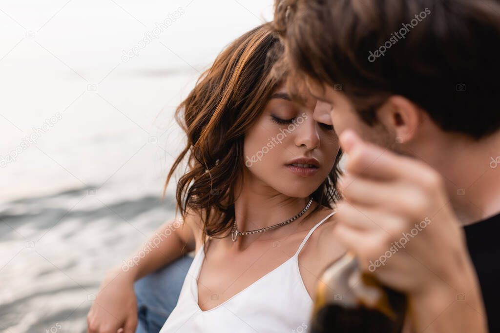 Selective focus of woman holding bottle of wine near boyfriend and sea  