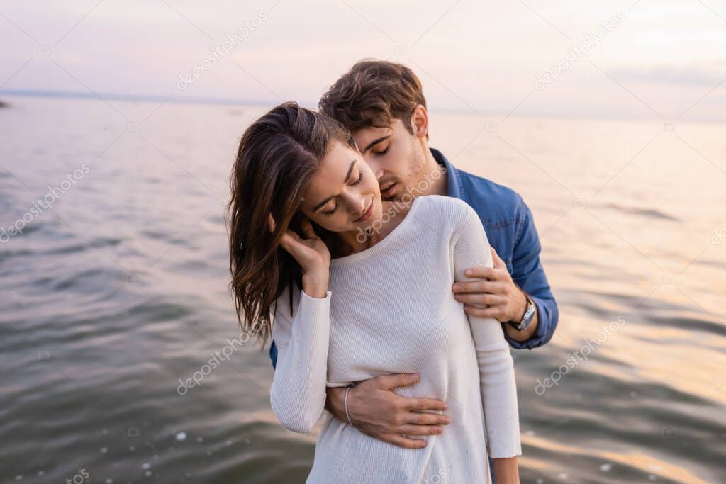 Man kissing neck and hugging girlfriend near sea at evening 