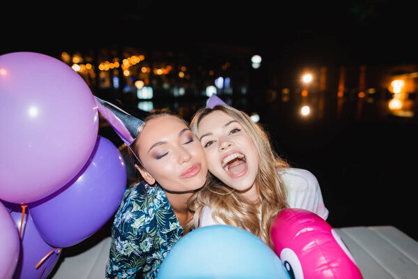 Selective focus of young women in party caps near balloons at night 