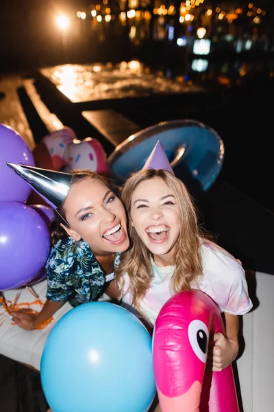 Jovens Mulheres Olhando Para Câmera Perto Balões Durante Festa Noite — Fotografia de Stock