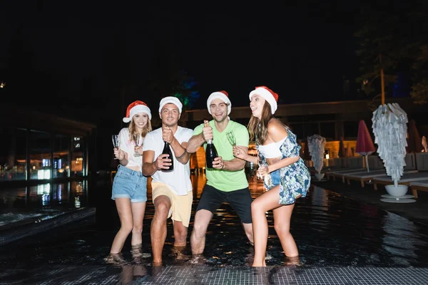 Vänner Santa Hattar Med Glasögon Och Champagne Flaskor Poolen Natten — Stockfoto