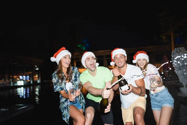 Focus Selettivo Amici Eccitati Cappelli Babbo Natale Champagne Apertura Vicino — Foto Stock