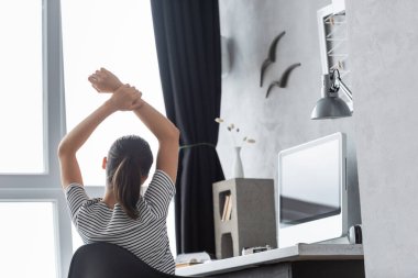 Masadaki bilgisayarın yanında oturan genç tele-işçinin arka görüntüsü 