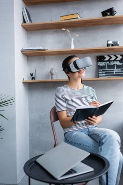 Sehpanın yanındaki dizüstü bilgisayara yazarken VR kulaklık kullanan seçici bir tele-muhabir. 