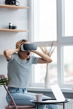 Heyecanlı bir kadının evdeki kahve sehpasının yanında vr kulaklık ve defter kullanarak seçici odak noktası 