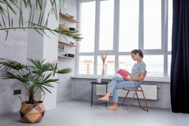 Çıplak ayaklı bir kadının evdeki kahve masasında kitap okumasının seçici odağı. 