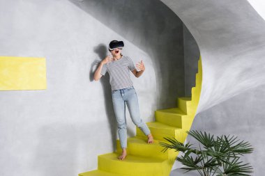 VR başlıklı heyecanlı kadın evdeki merdivenlerde duruyor. 