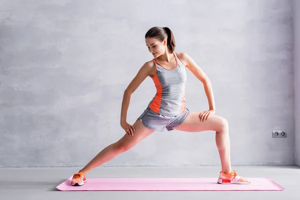 在灰色背景下伸展在健身垫上的女运动员 — 图库照片