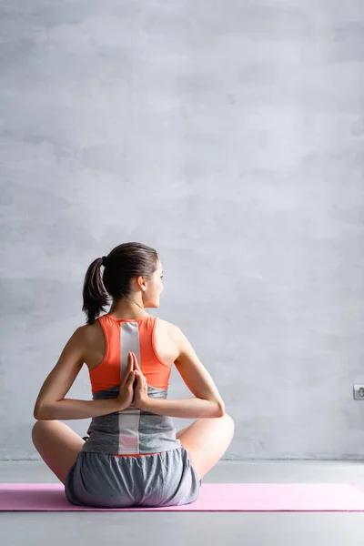 Back view of woman with prayer hands looking away on fitness mat