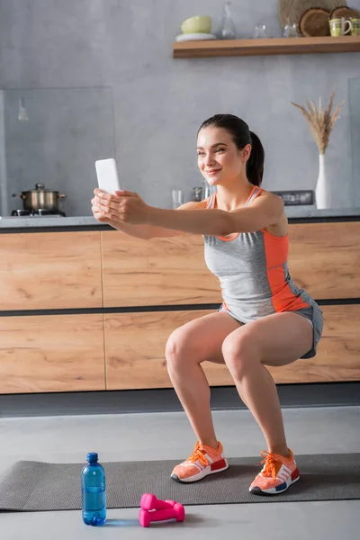 Selektiv Fokus Idrottskvinna Gör Squat Samtidigt Hålla Smartphone Nära Vatten — Stockfoto