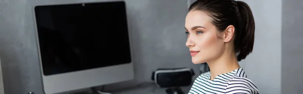 Panoramic shot of freelancer looking away near computer monitor at home