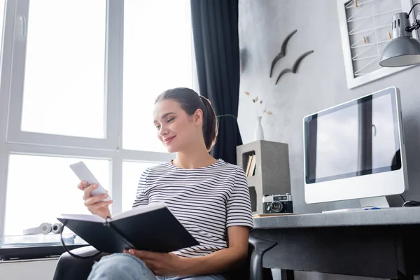 Selective Focus Brunette Freelancer Using Smartphone Holding Notebook Computer Table — Stock Photo, Image