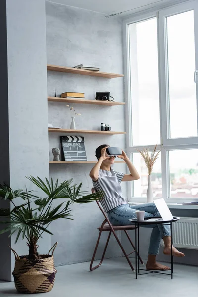 在家里的咖啡桌上 赤脚自由职业者在笔记本电脑和杯子旁边使用Vr耳机 — 图库照片